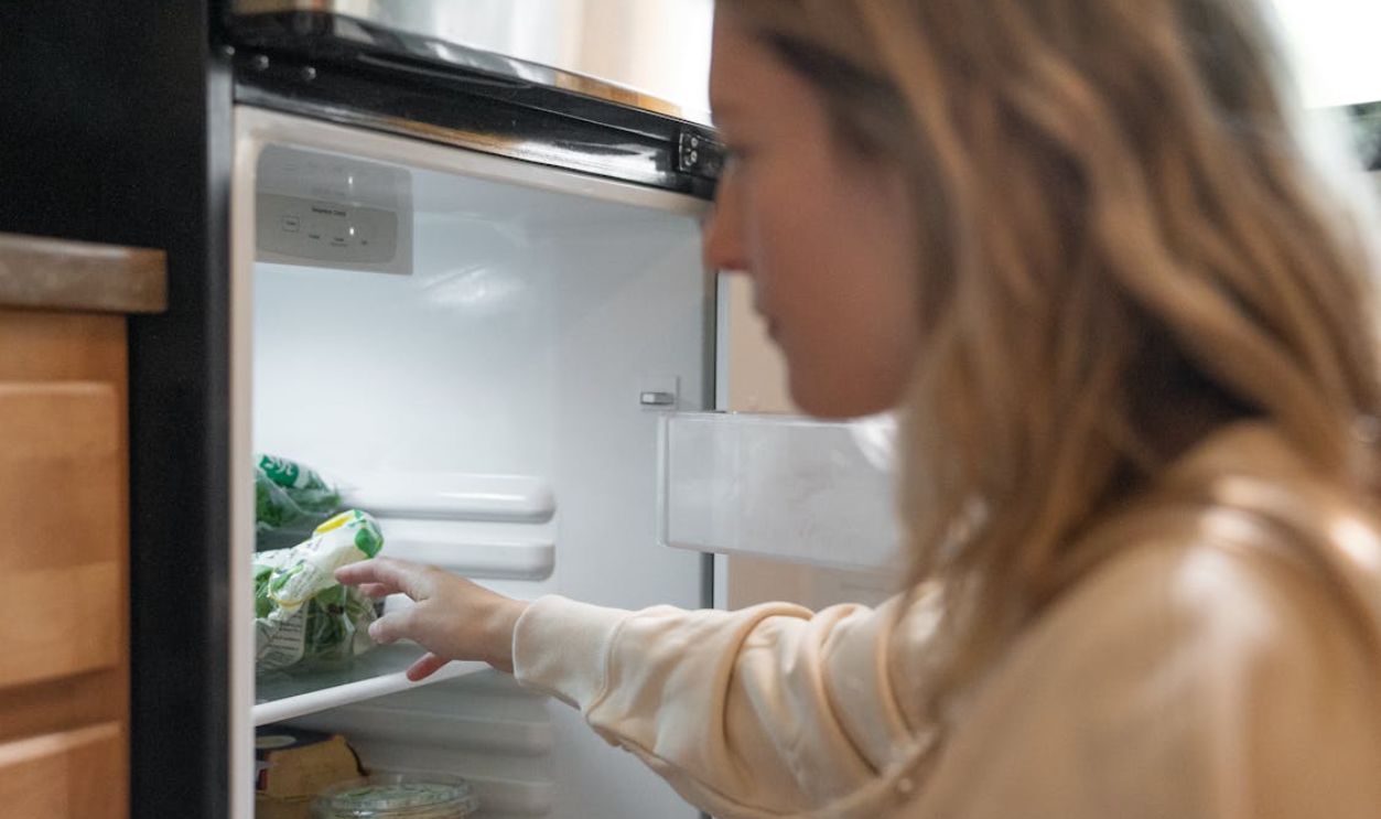 Woman grabbing vegetables from a refrigerator, symbolizing healthy living.