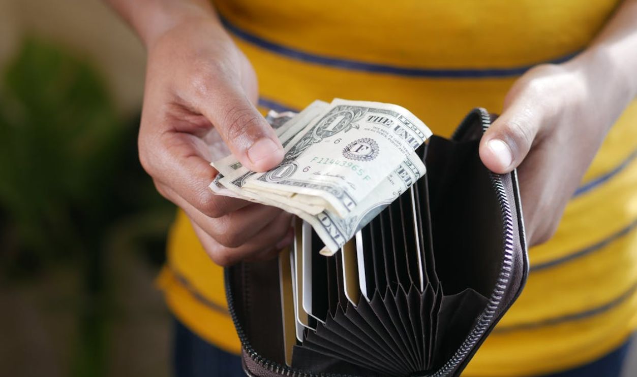 Close-up of a person's hands holding US dollar bills and a wallet.
