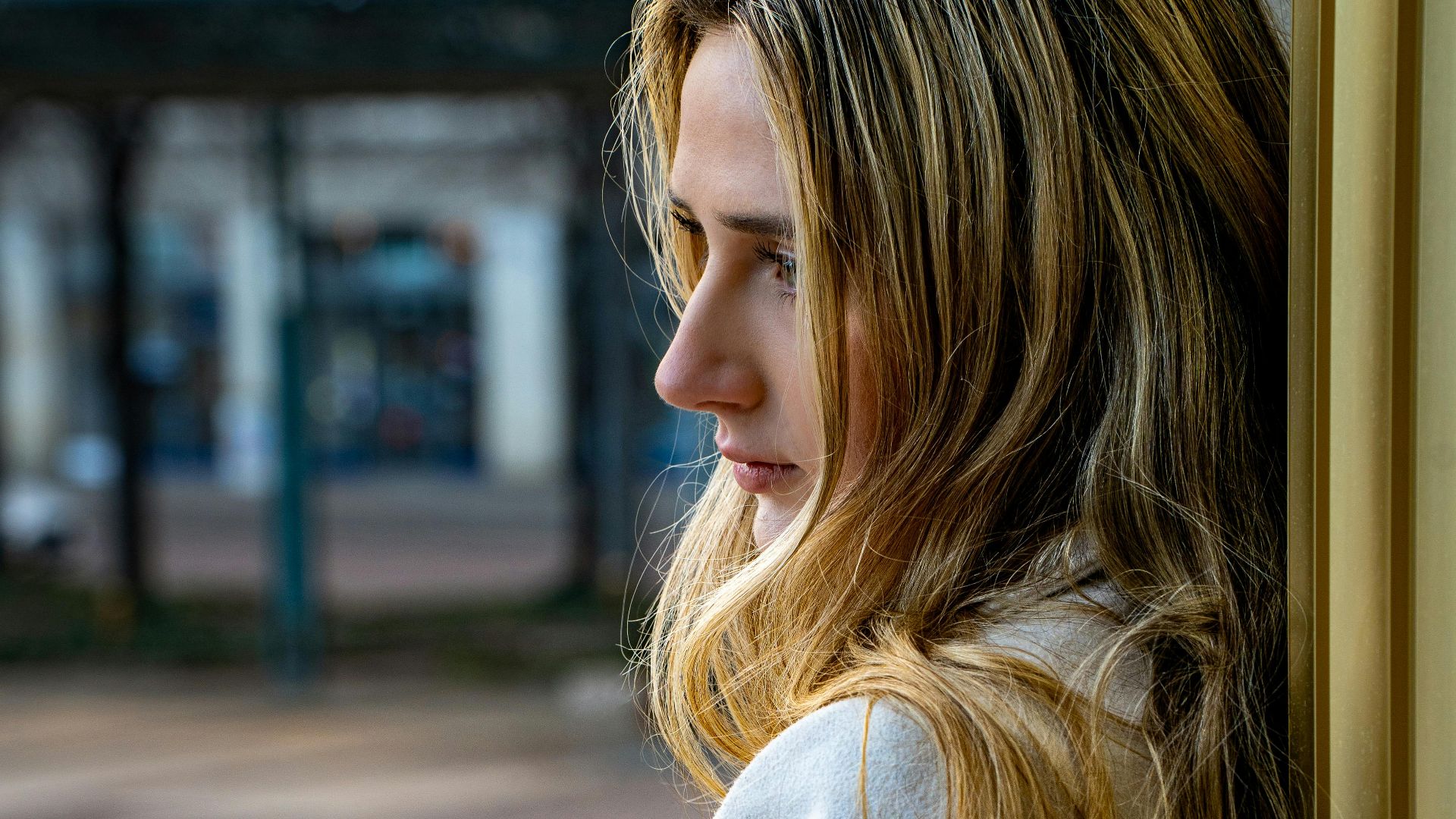 Profile portrait of a woman leaning against a wall in an urban setting, lost in contemplation.