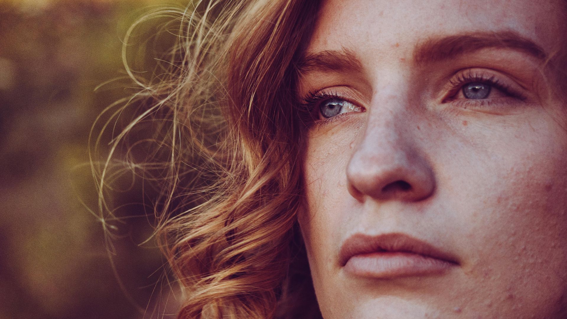 Close-up portrait of a young woman with curly hair and blue eyes, exuding calmness.