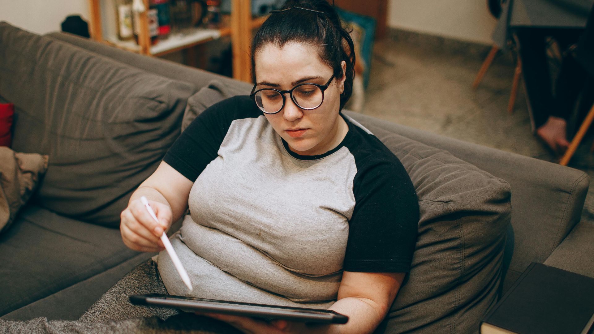 Woman relaxing on a couch while using a digital tablet stylus, ideal for remote work or casual browsing.