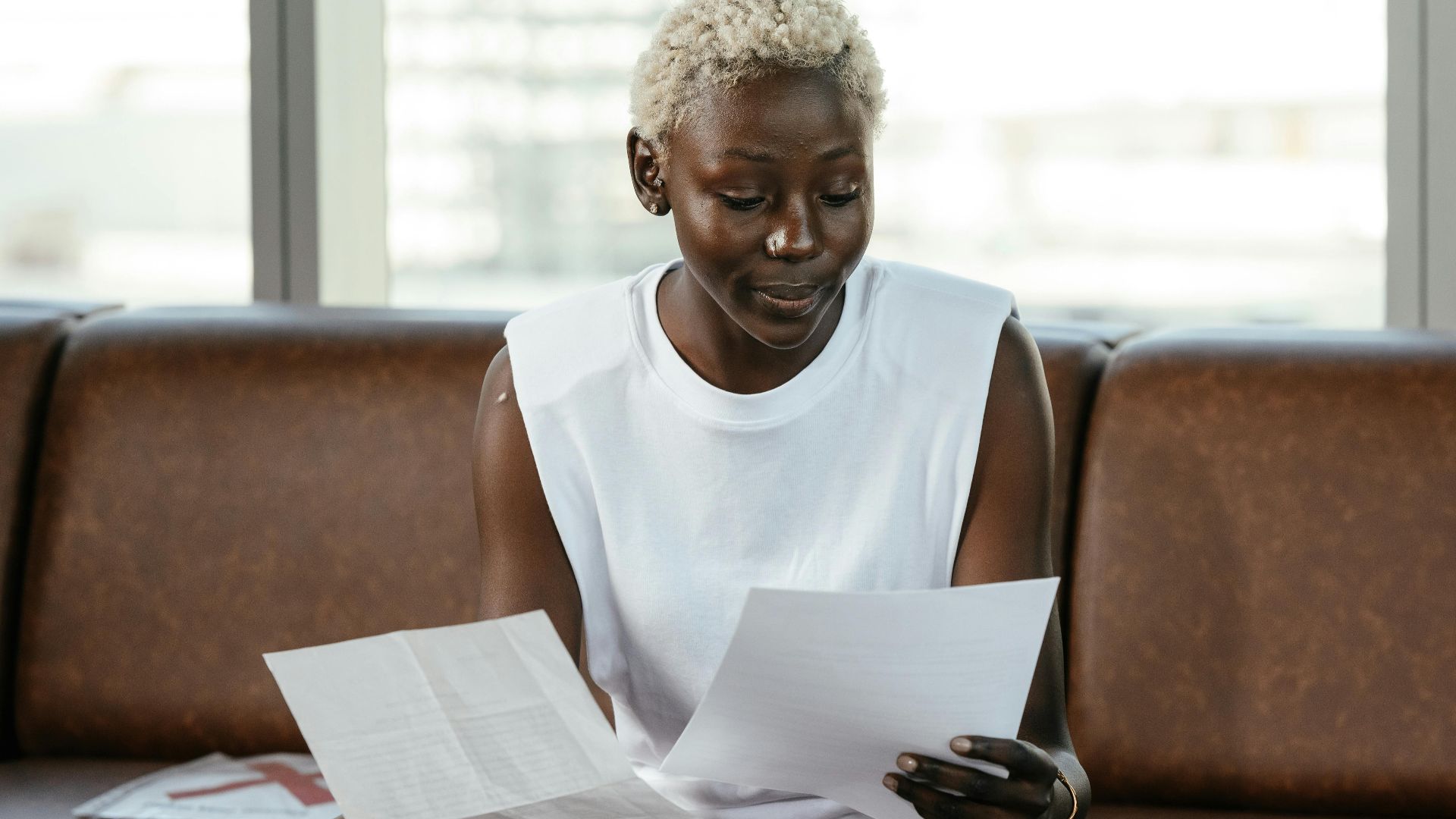 Concentrated African American female comparing important papers of report on leather sofa in office