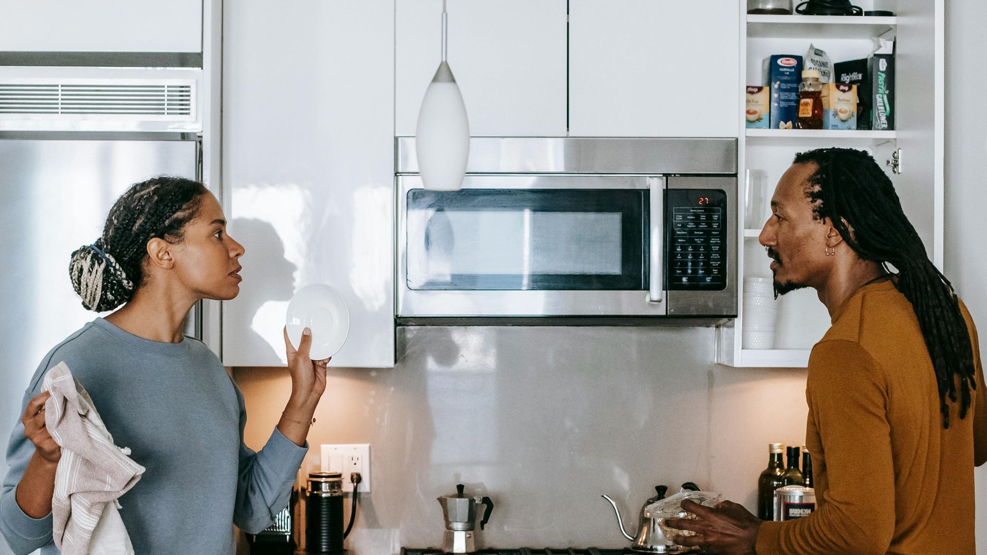 Young black woman talking to annoyed male partner while looking at each other during quarrel in house