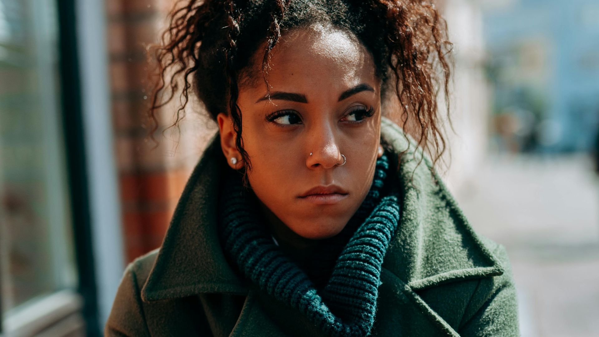 Stylish woman in a green coat stands confidently on a city street, showcasing urban fashion.