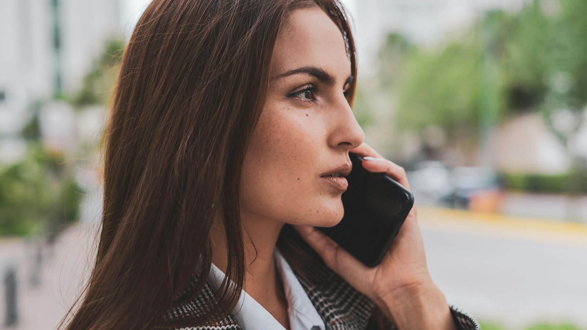 Confident businesswoman with brown hair talking on smartphone outdoors.