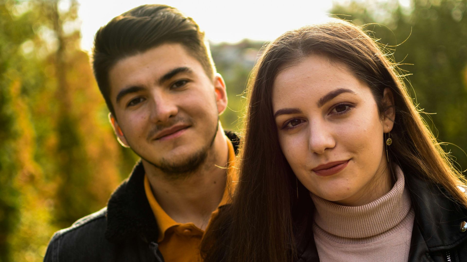 Young couple enjoying a sunny day outdoors with green trees in the background.