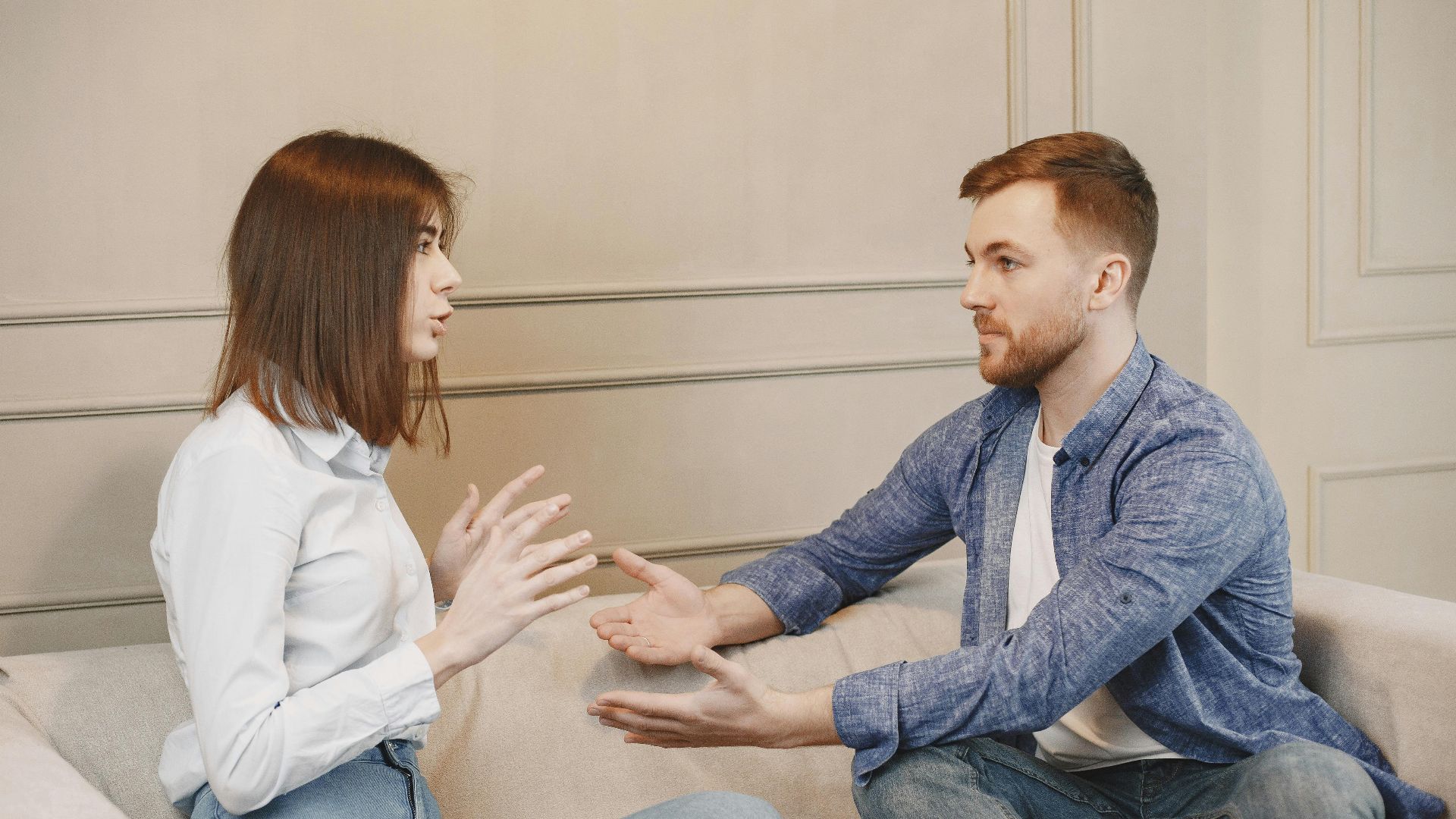 A young couple sitting on a couch having a thoughtful conversation with expressive hand gestures.