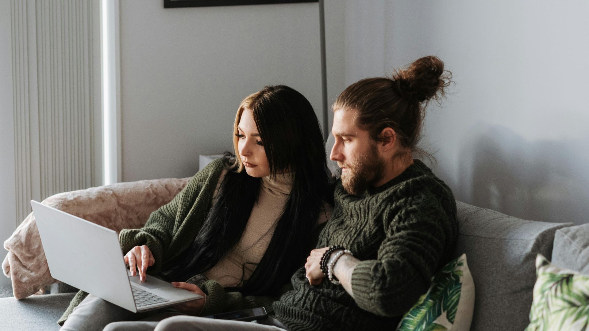 Young woman with hipster boyfriend browsing internet on netbook while resting on soft couch at home