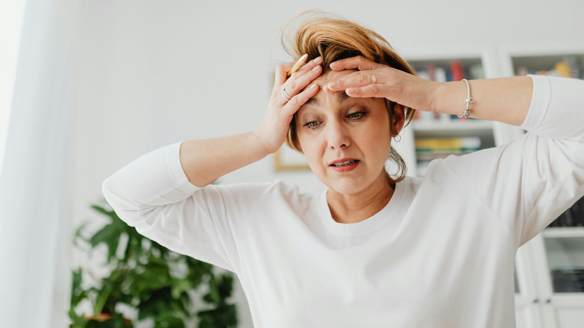 A worried woman indoors with hands on forehead, expressing stress.