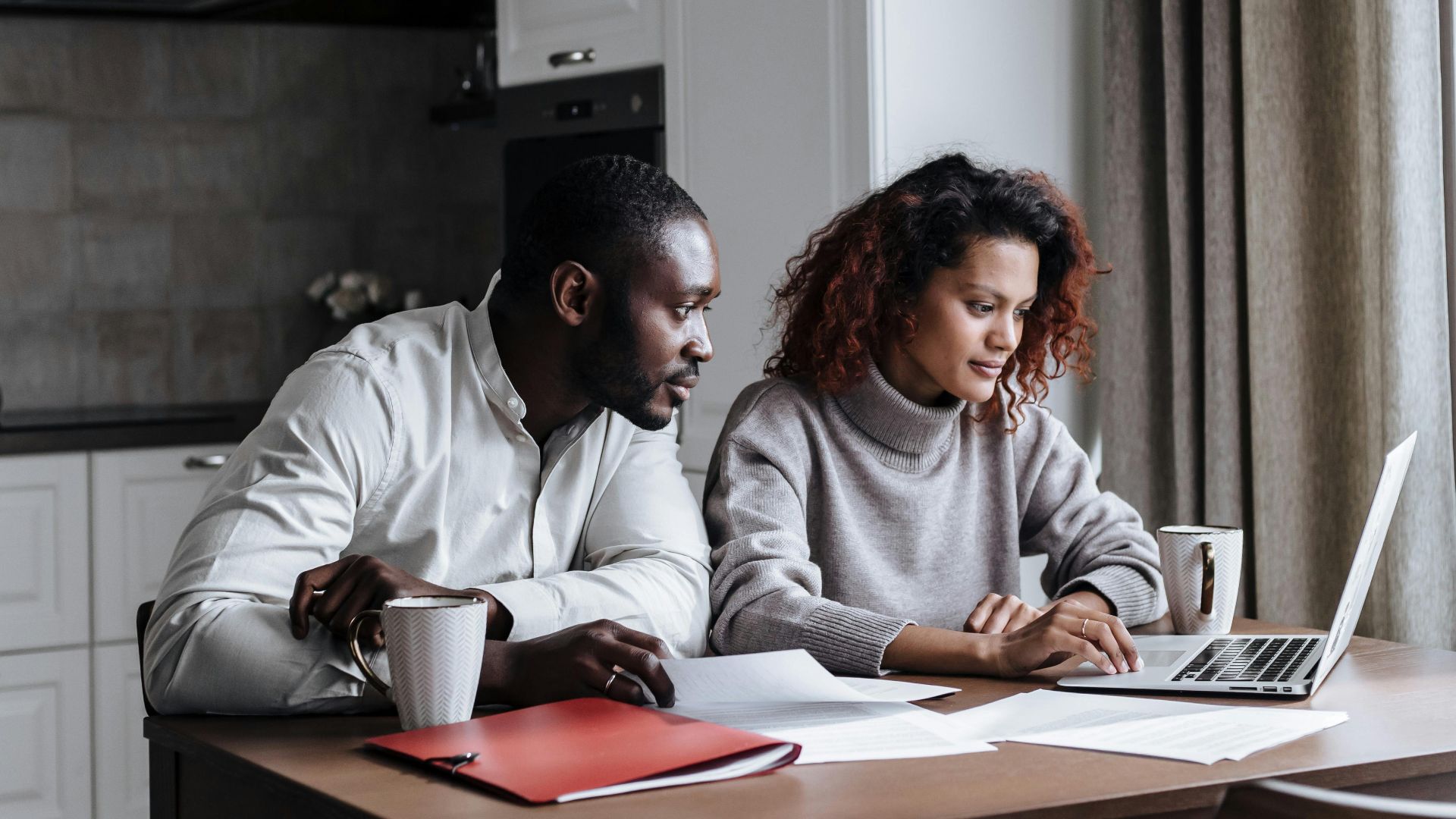 A diverse couple working together on a laptop in a modern kitchen setting, displaying teamwork and collaboration.