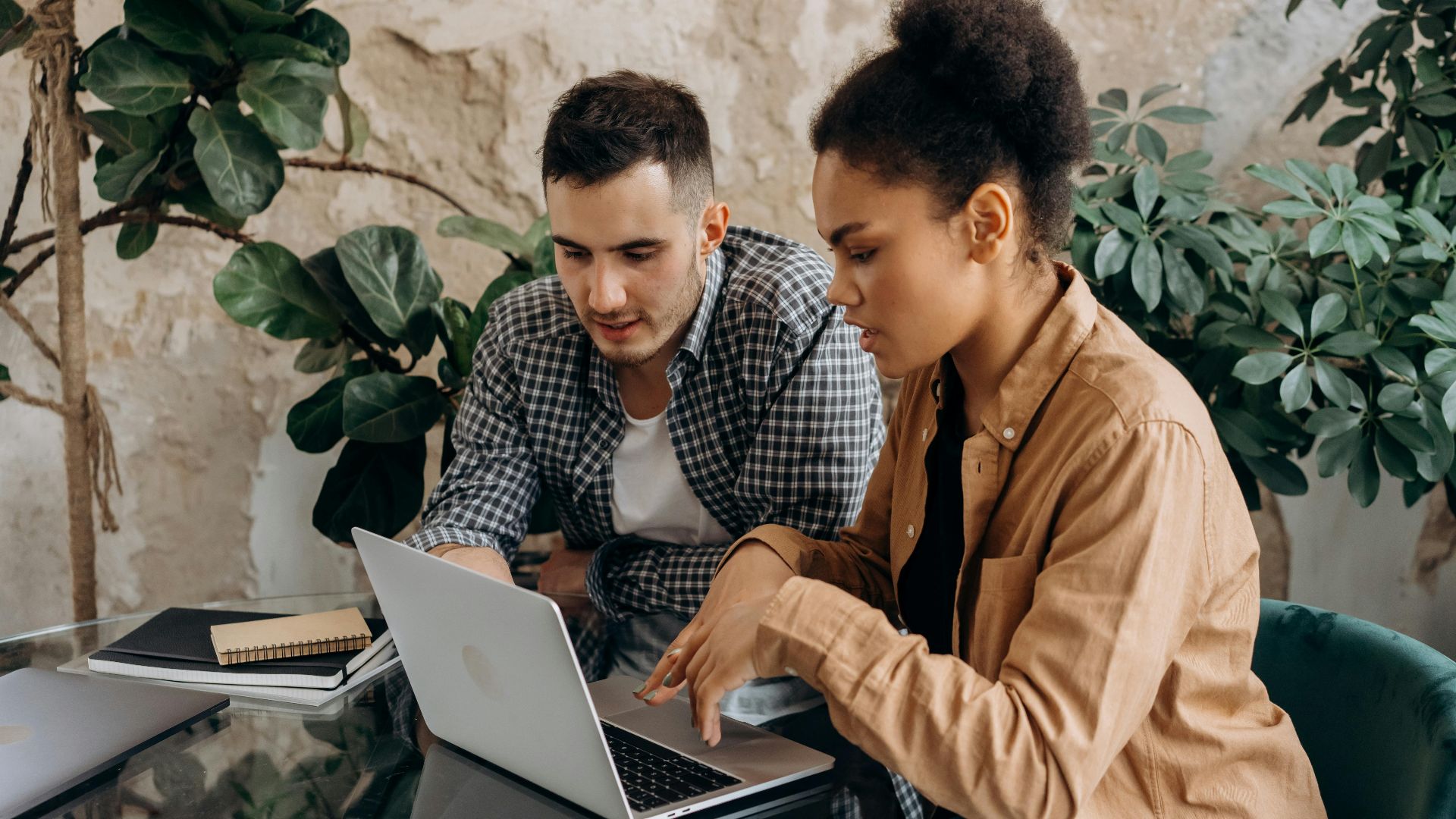Two colleagues working together on a laptop in a modern office setting.