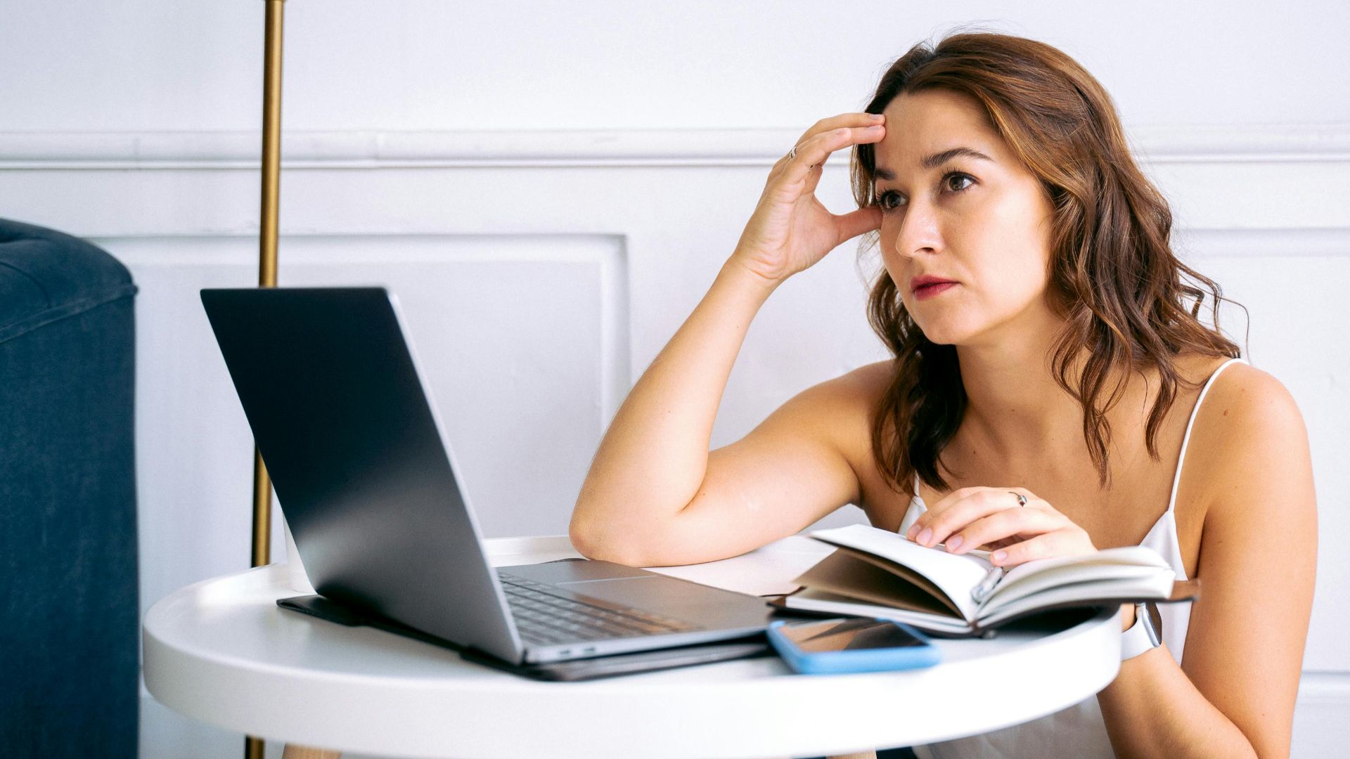 A stressed woman sitting at a desk with a laptop and notebook, reflecting work burnout.