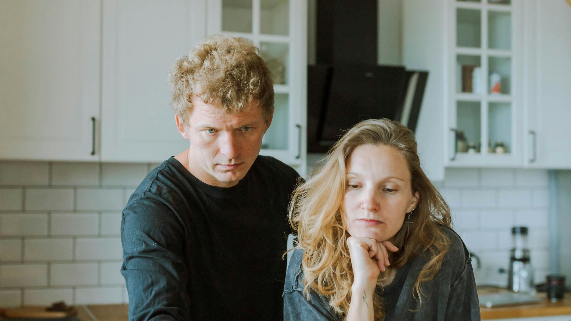 Man and woman focused on laptop work in a bright, modern kitchen setting.