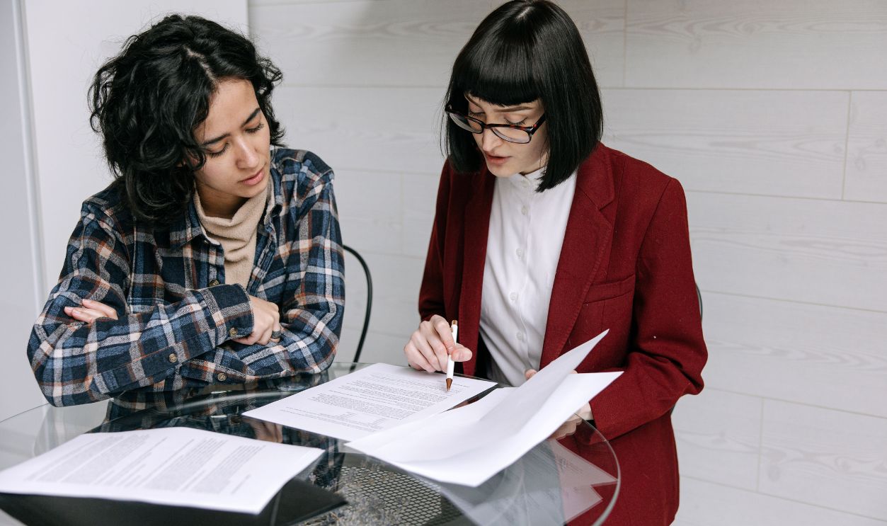 Two women collaborating at a glass table, reviewing business documents 