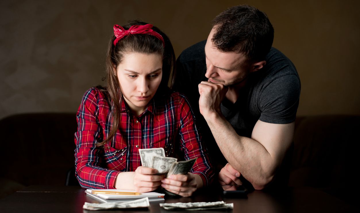 A woman counts family money, a man stands next to her and supports her