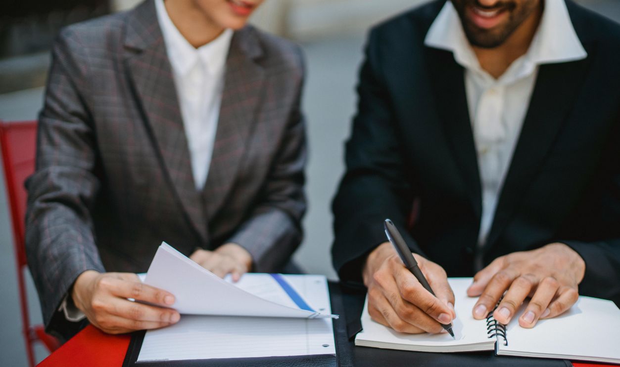Two business professionals in suits reviewing documents and writing notes at a table