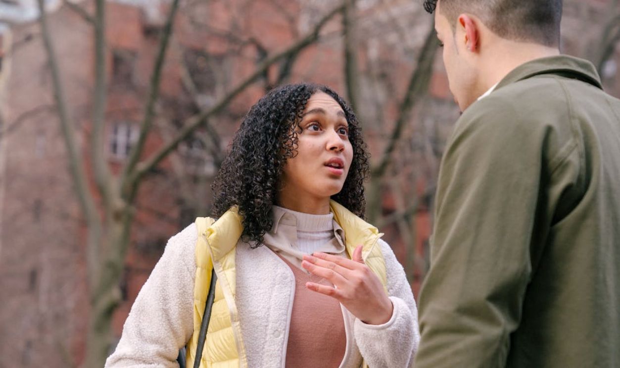 A young couple engaged in a serious conversation on a city street with trees in the background