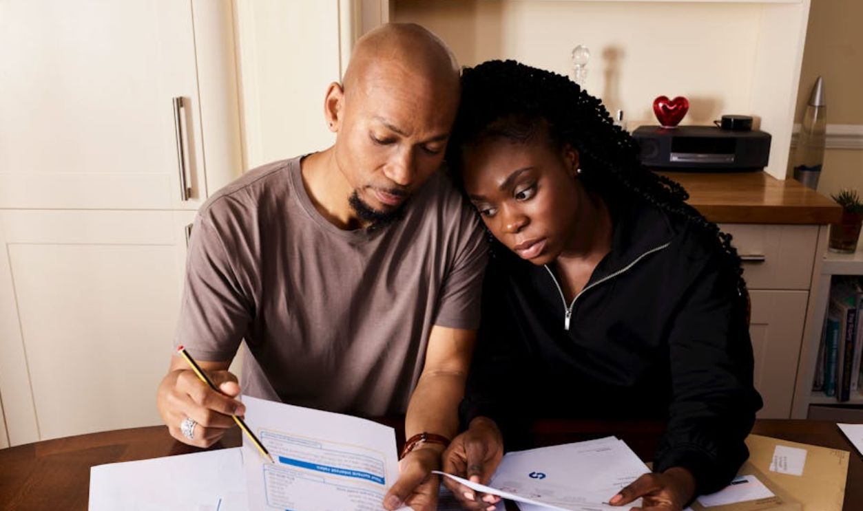 A couple sitting at a table reviewing financial documents, highlighting domestic budgeting
