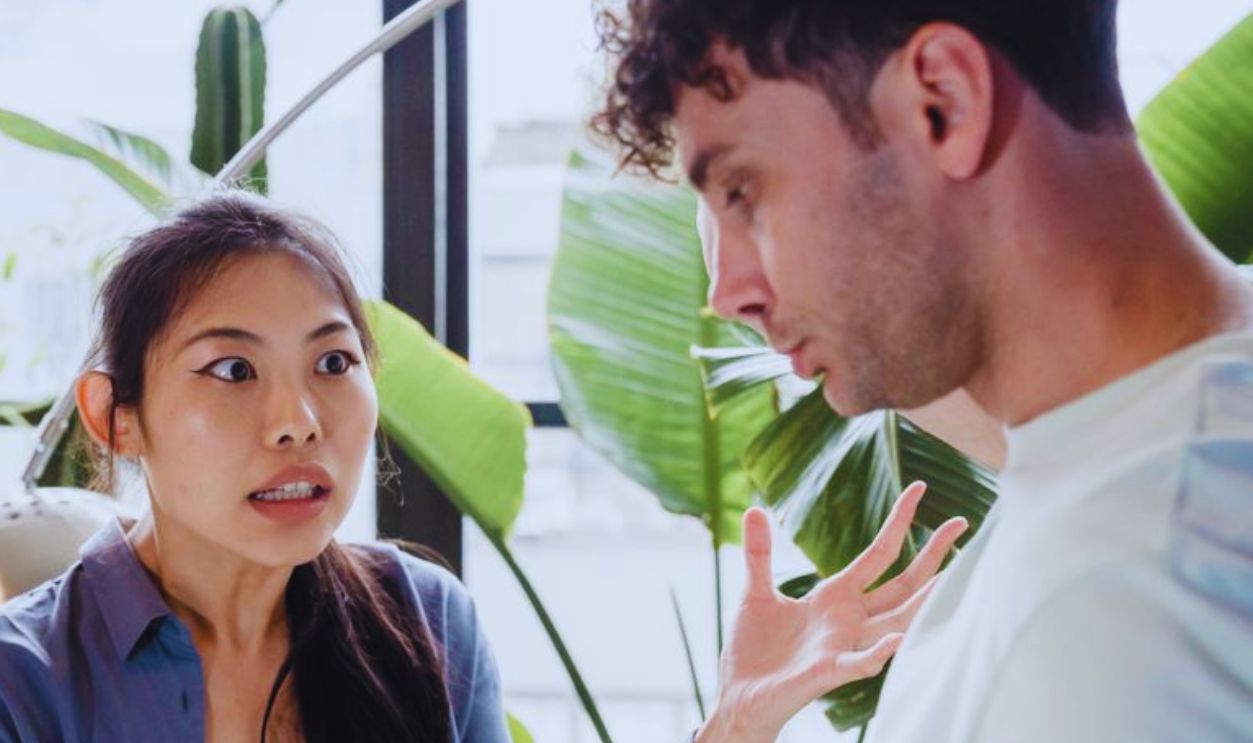 A couple engaged in a heated discussion indoors surrounded by plants, expressing emotions