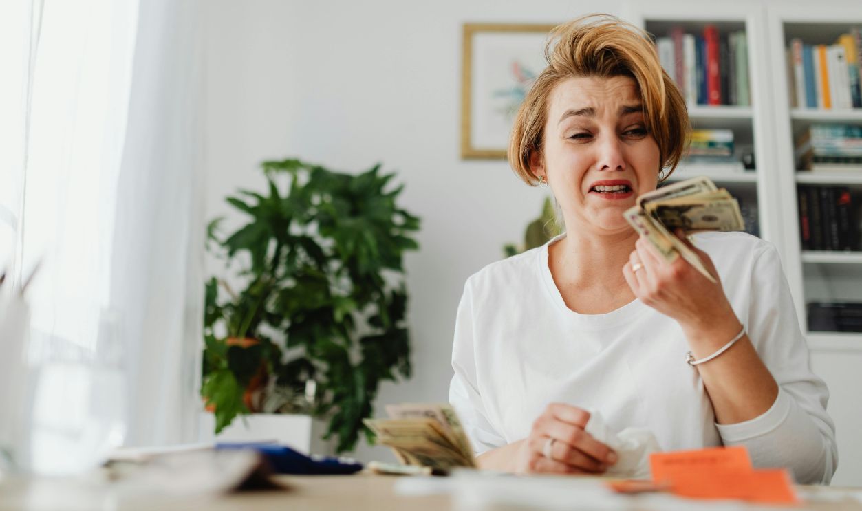 A woman looking stressed while counting money in a living room setting