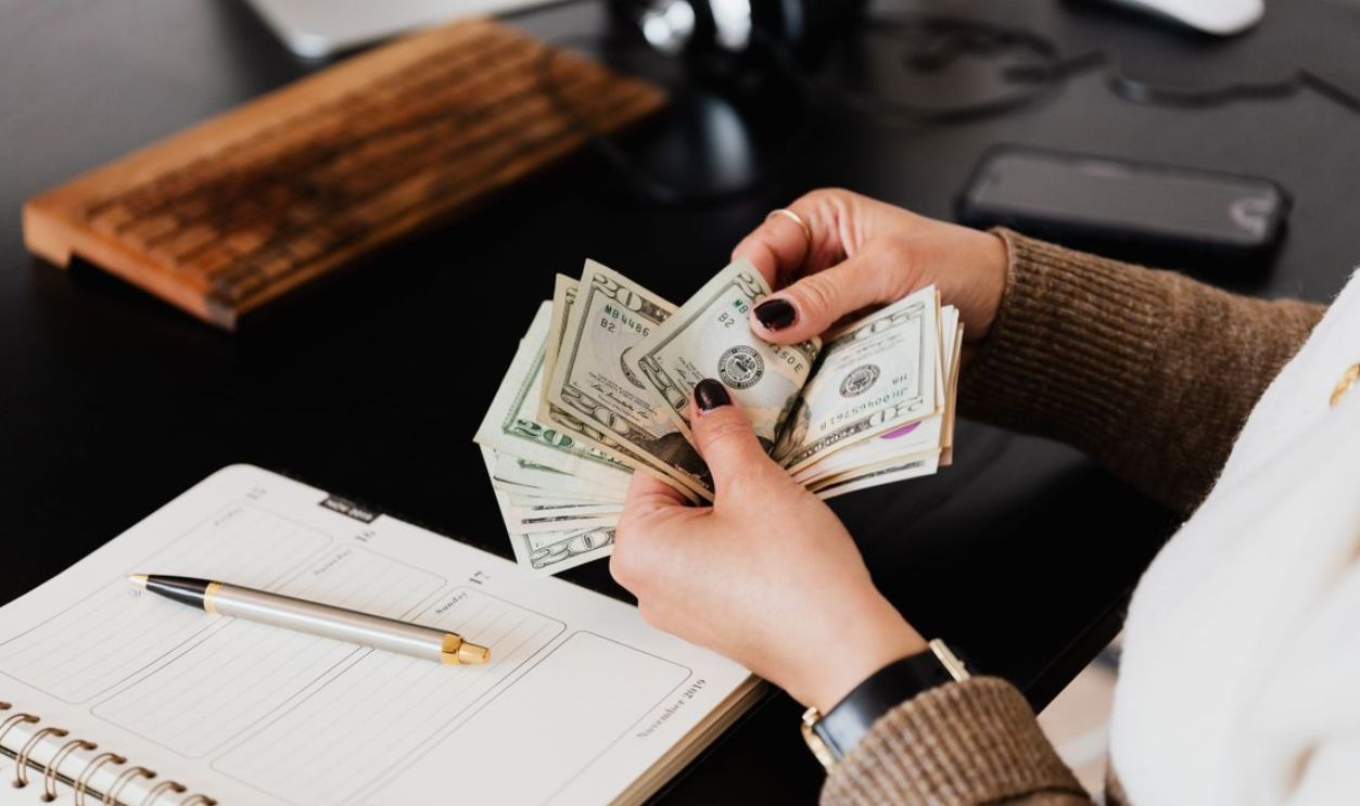 Person counting cash with a planner and gold pen on a desk, representing financial management