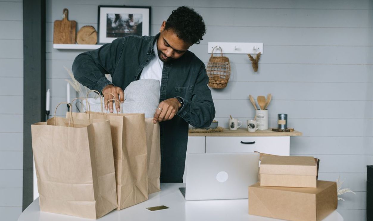 Young man organizing paper bags near a laptop in a cozy indoor setting.