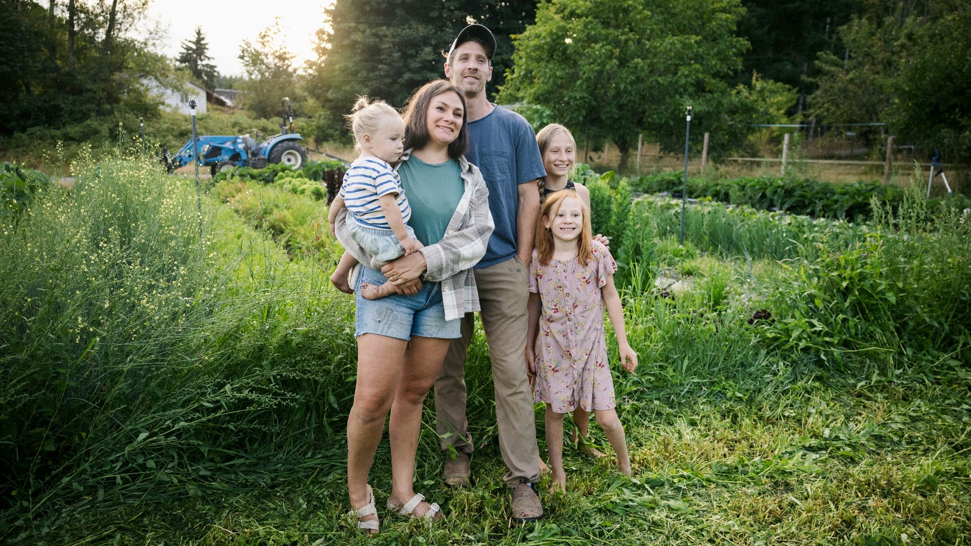 Family standing in a lush green field with tractor.