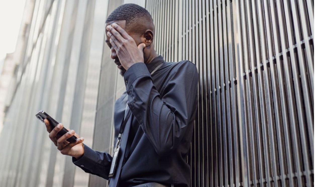 A worried businessman in formal attire using a smartphone outside a modern building.
