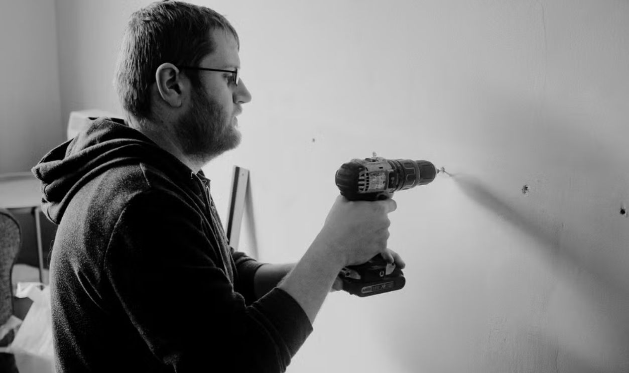 Man using a power drill to repair a wall inside a home. Black and white photo