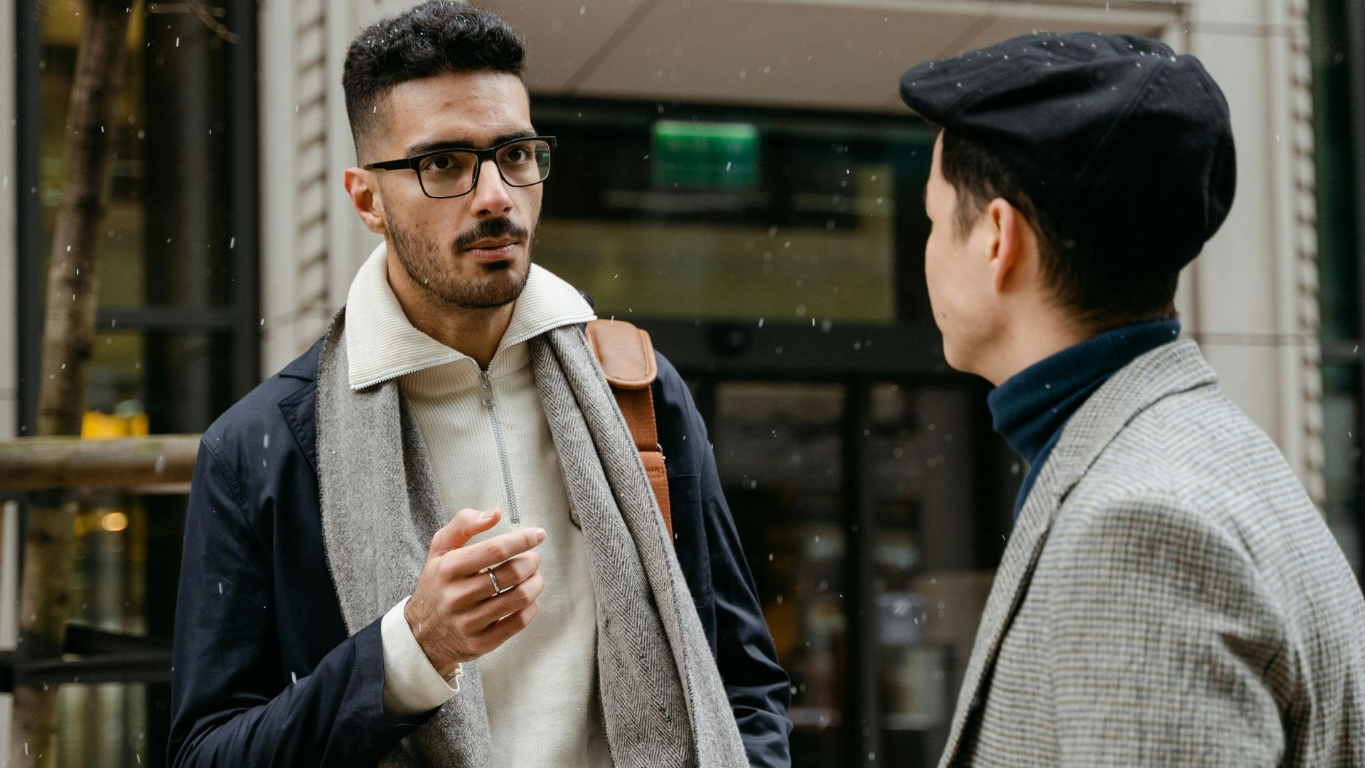 Two businessmen engaged in conversation outside in winter attire with snow falling lightly