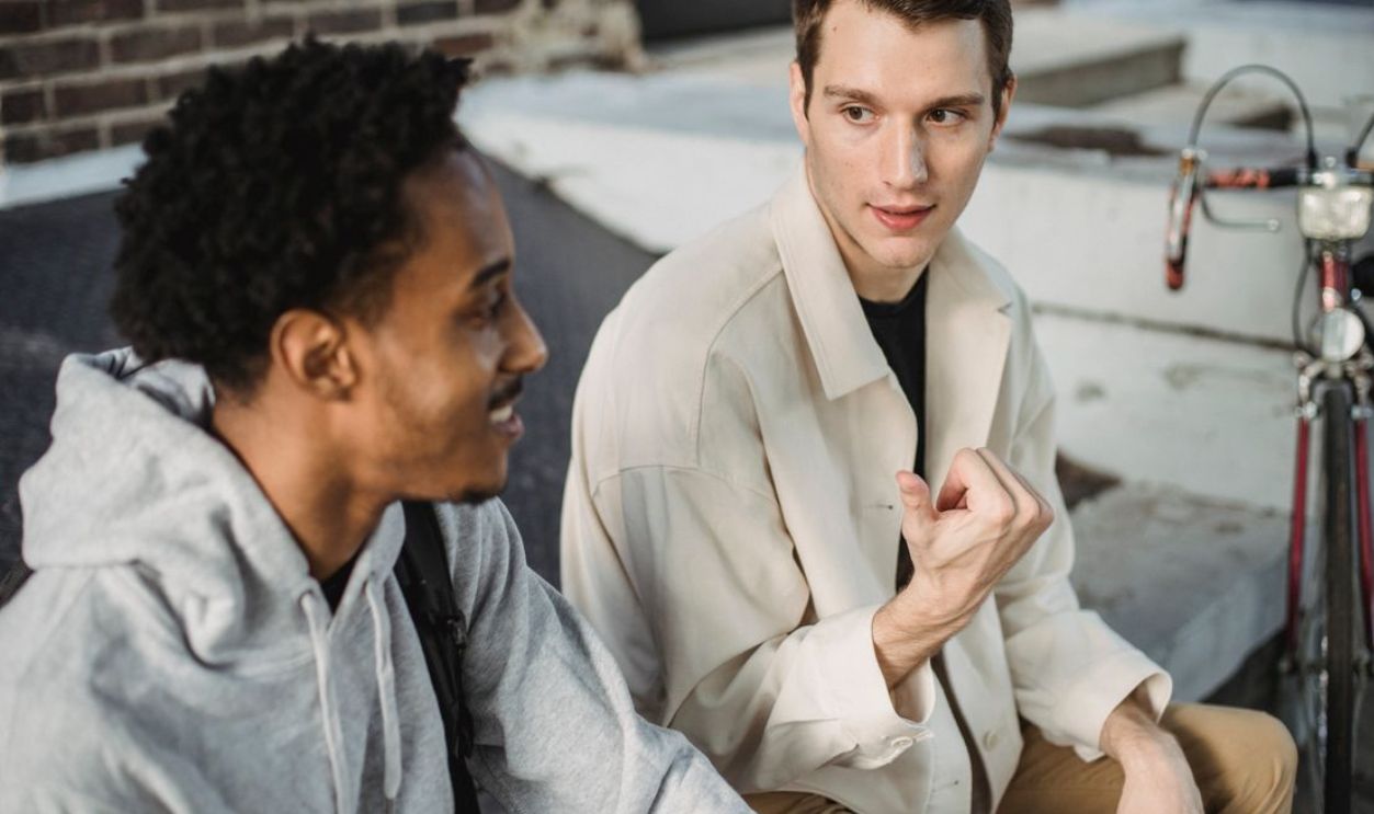 Two young men having a lively conversation outdoors on a sunny day with a bicycle nearby