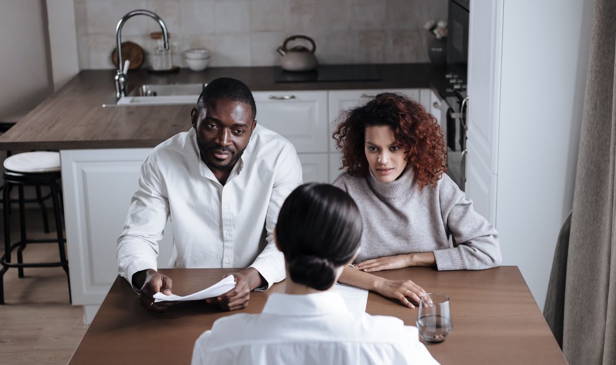 A couple attentively listens to an advisor during a meeting in a modern kitchen