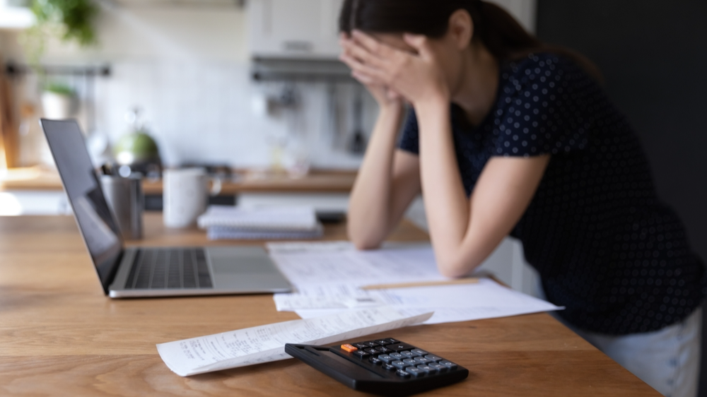 Close up view calculator and bills on table, desperate young woman on background, makes expenses and earnings analysis feels tired and disappointed. Lack of money, overspend, debt, financial troubles