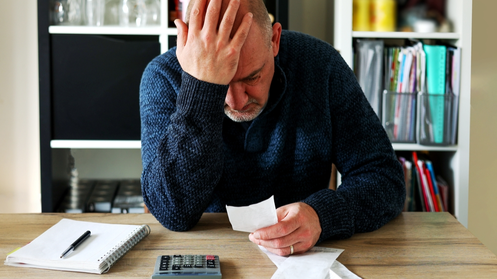 Man upset sitting on a table holding his head and calculating