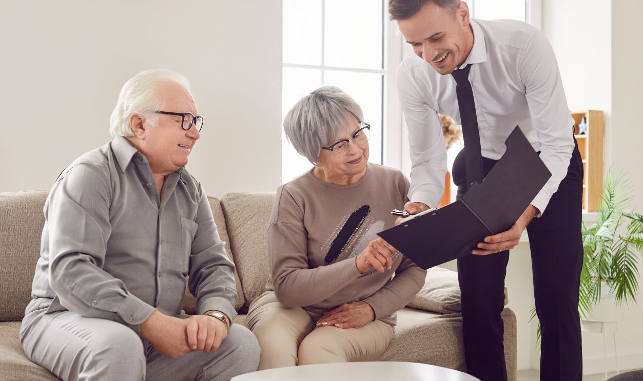 Gray-haired confident senior couple sitting on sofa in the living room at home and having consultation with a male financial advisor about health insurance. Investment in retirement concept