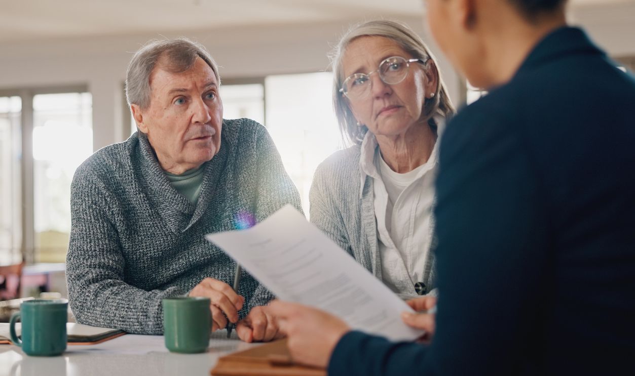 Shutterstock-2520695661, Conversation, documents and senior couple with financial advisor for retirement annuity saving account. Meeting, finance paperwork and elderly man and woman with investment banker for pension growth.