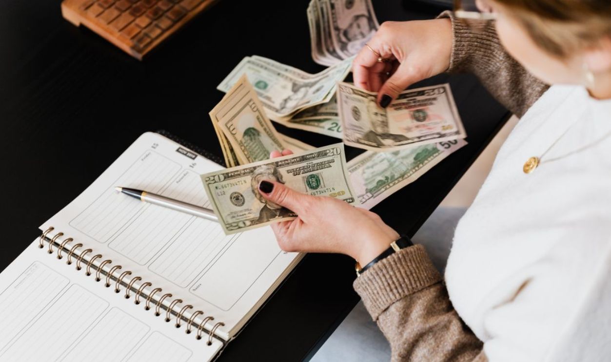 Woman organizing finances, counting dollar bills at desk with open notebook