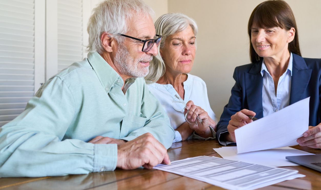 Shutterstock-2773351439, Retirement planning and financial protection — a senior couple is consulting with a professional financial advisor, reviewing paperwork and discussing estate and asset management.