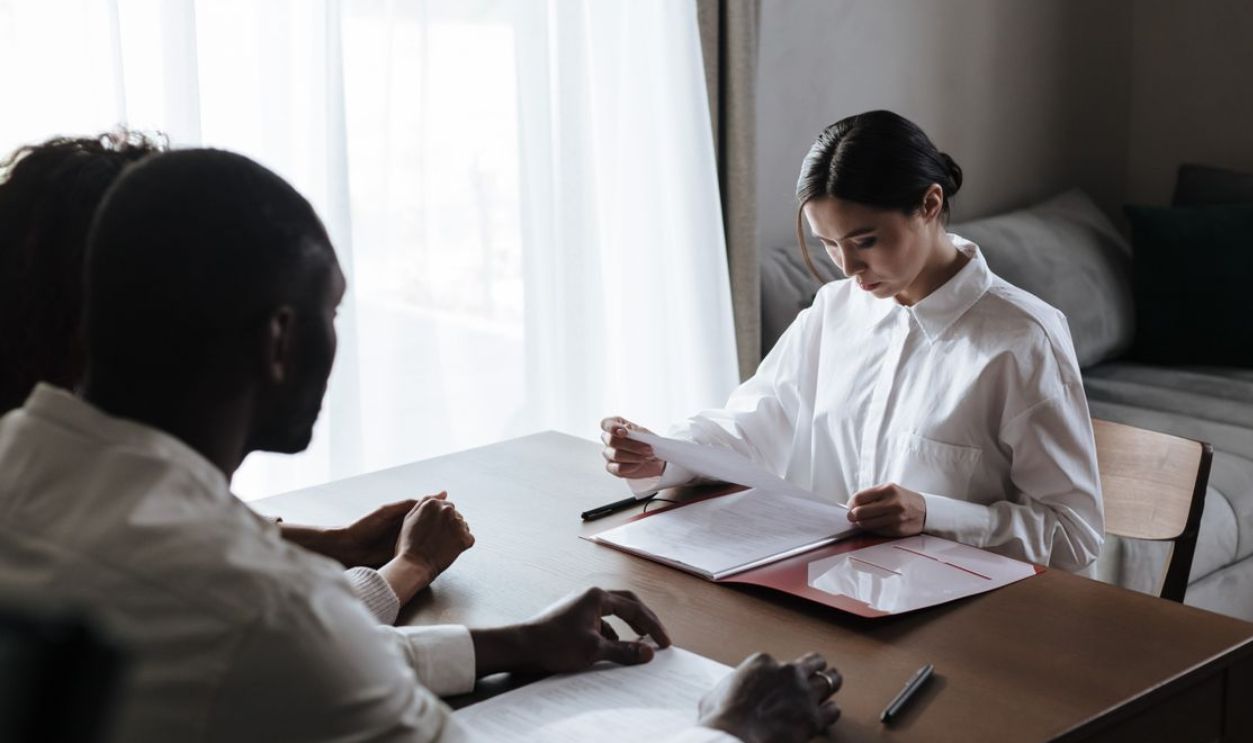 A professional woman reviews documents with a couple at home, indicating a collaborative decision-making process.