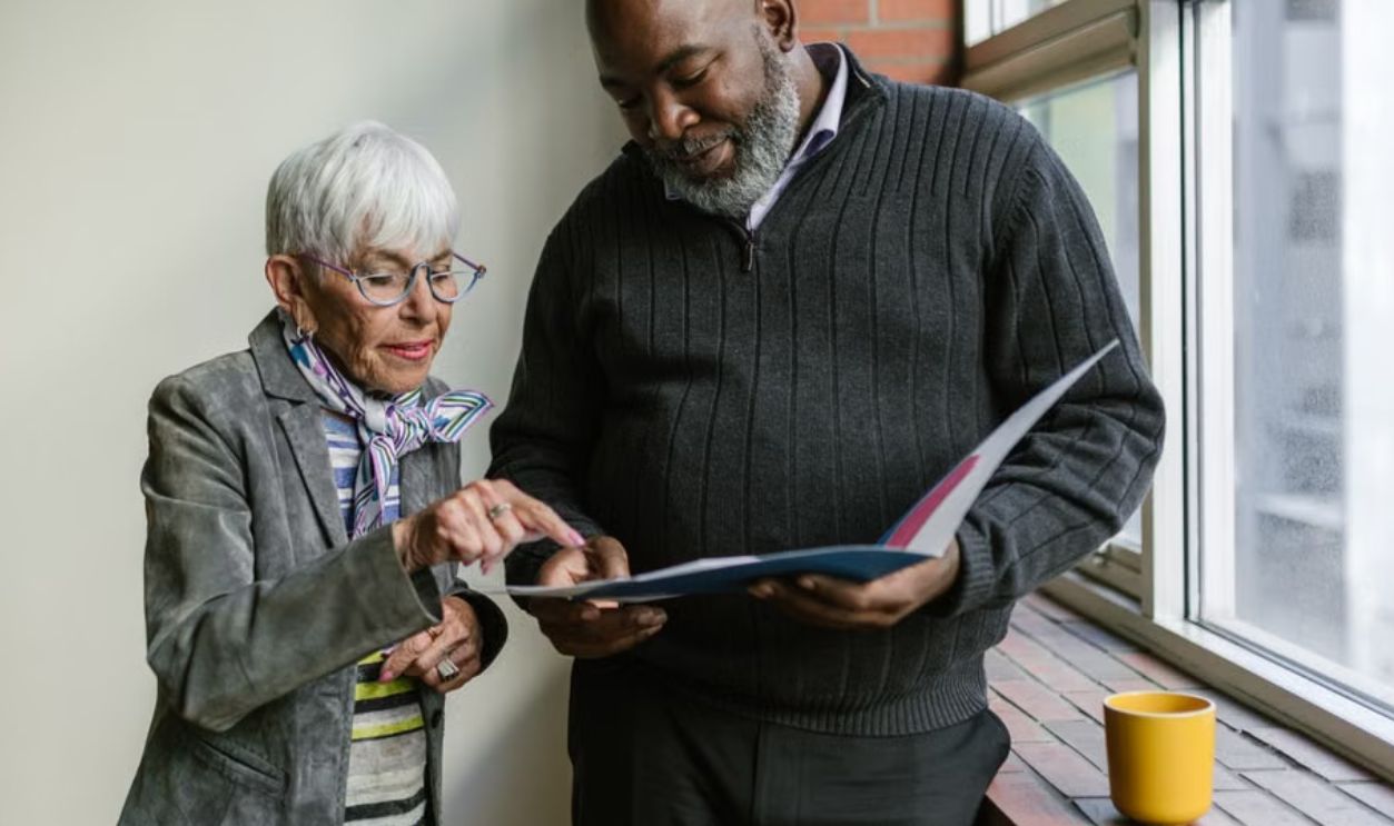 An elderly man and woman engage in a business discussion, reviewing documents in an office setting
