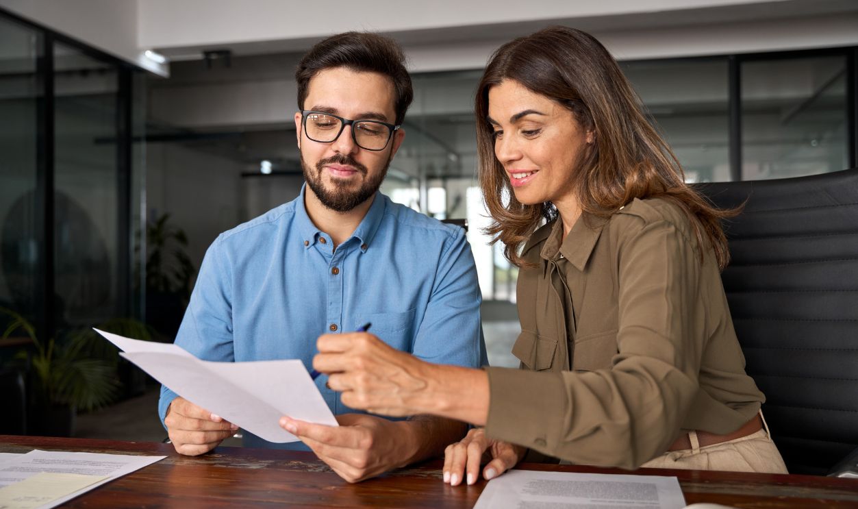 Shutterstock-2424450137, Smiling female financial advisor, attorney lawyer or bank manager consulting client investor reading document at business meeting reviewing legal paper file planning taxes working in office.