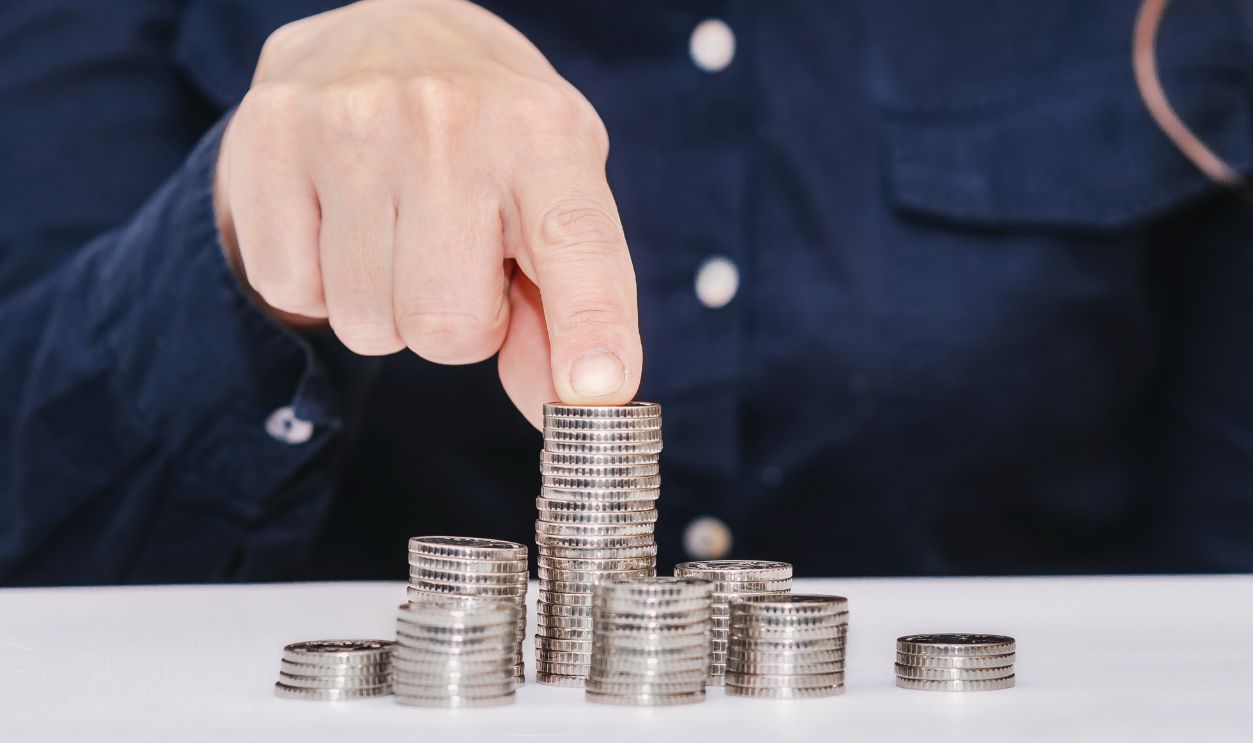 Stacks of coins on the table, finger holding the largest stack of coins