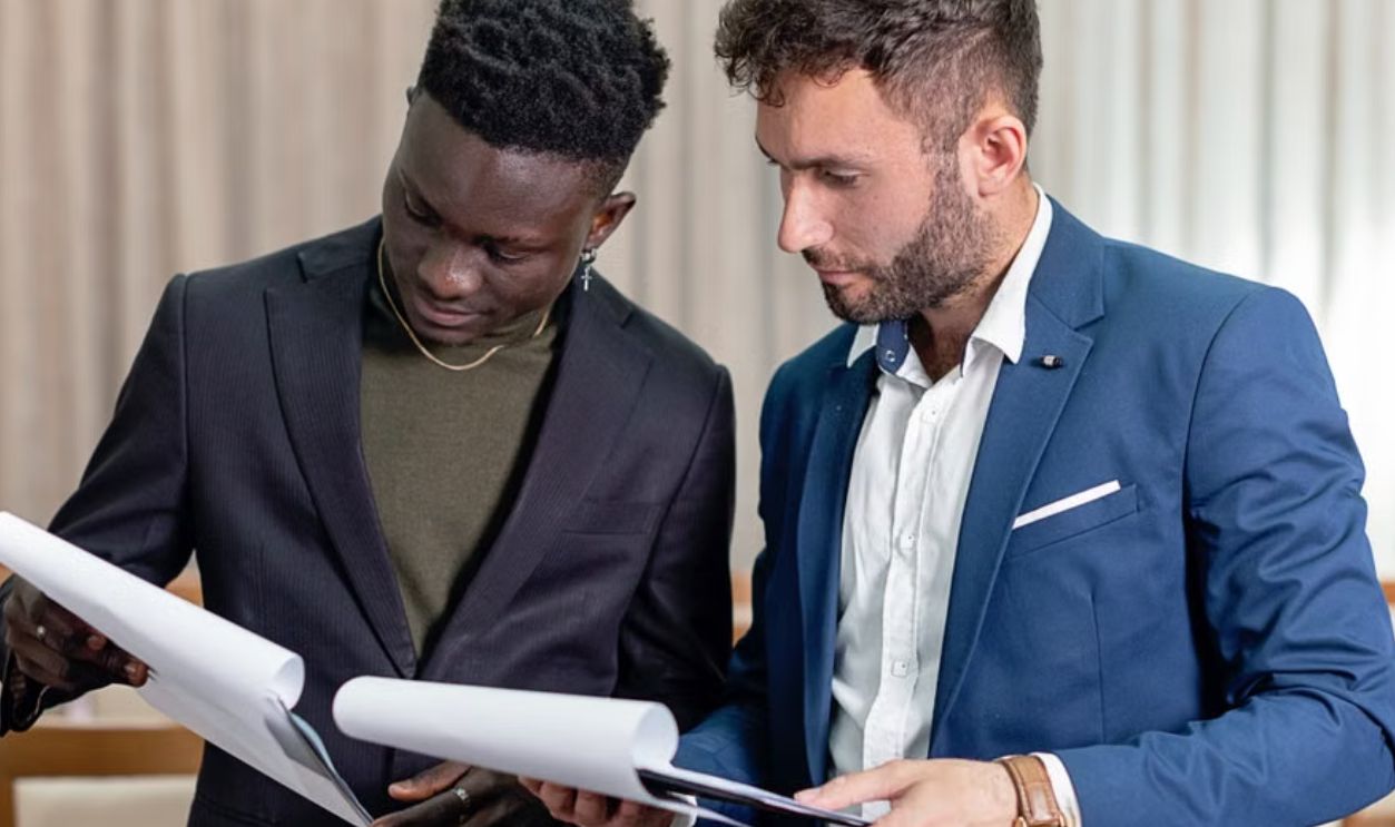 Two businessmen in suits reviewing contracts and business documents indoors