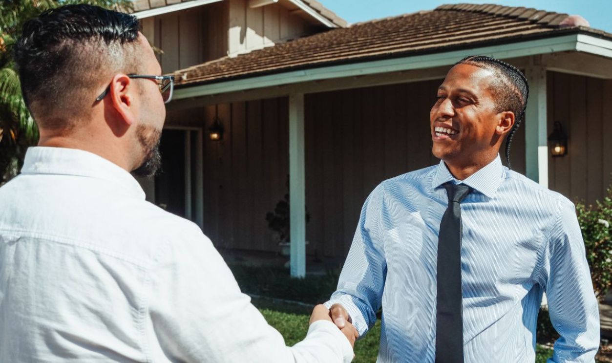 Two real estate professionals shaking hands in front of a new home during a transaction