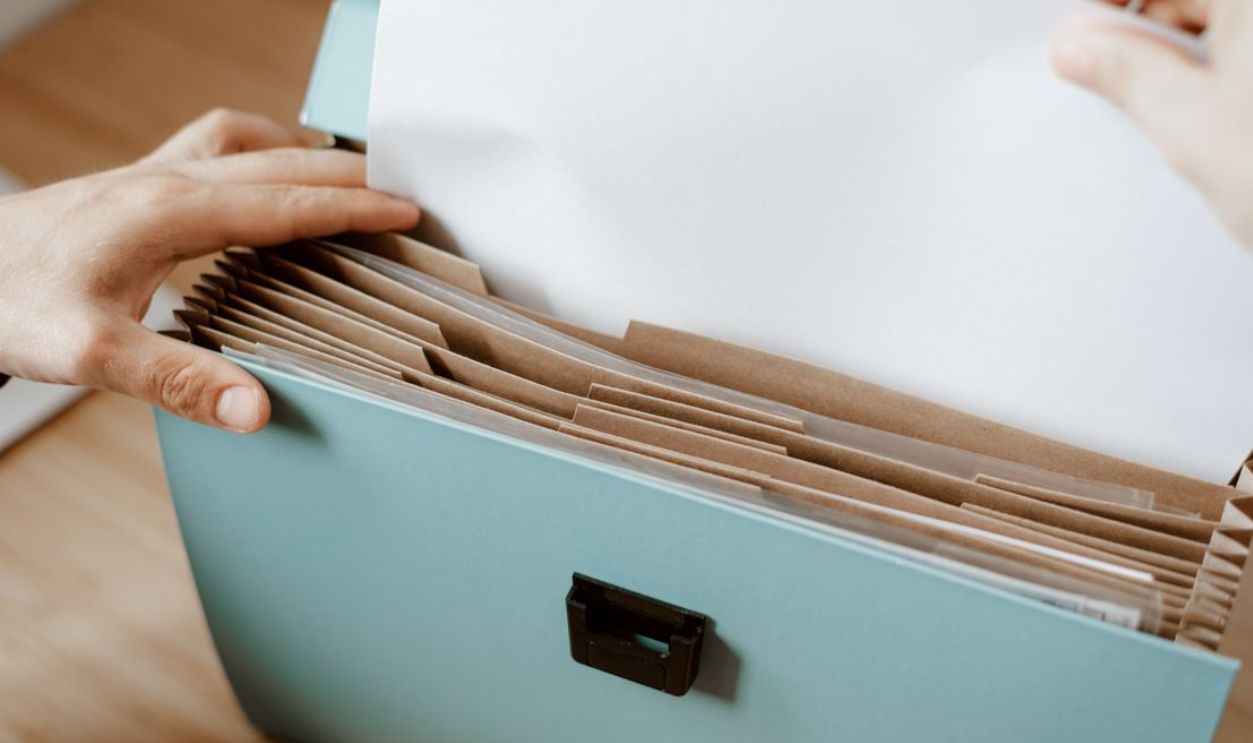 Hands organizing papers in a blue office folder with brown dividers, showing workplace efficiency.