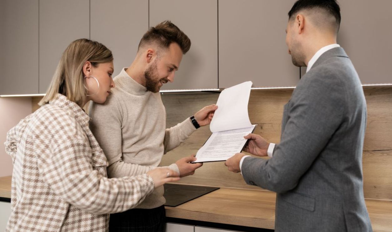 A couple reviews real estate documents with an agent in a modern indoor setting, discussing a potential property purchase