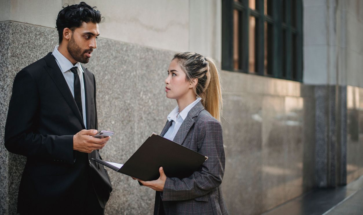 Two professionals in business attire discussing work outside an office