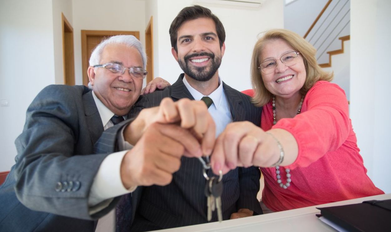 Smiling elderly couple receiving house keys from realtor indoors