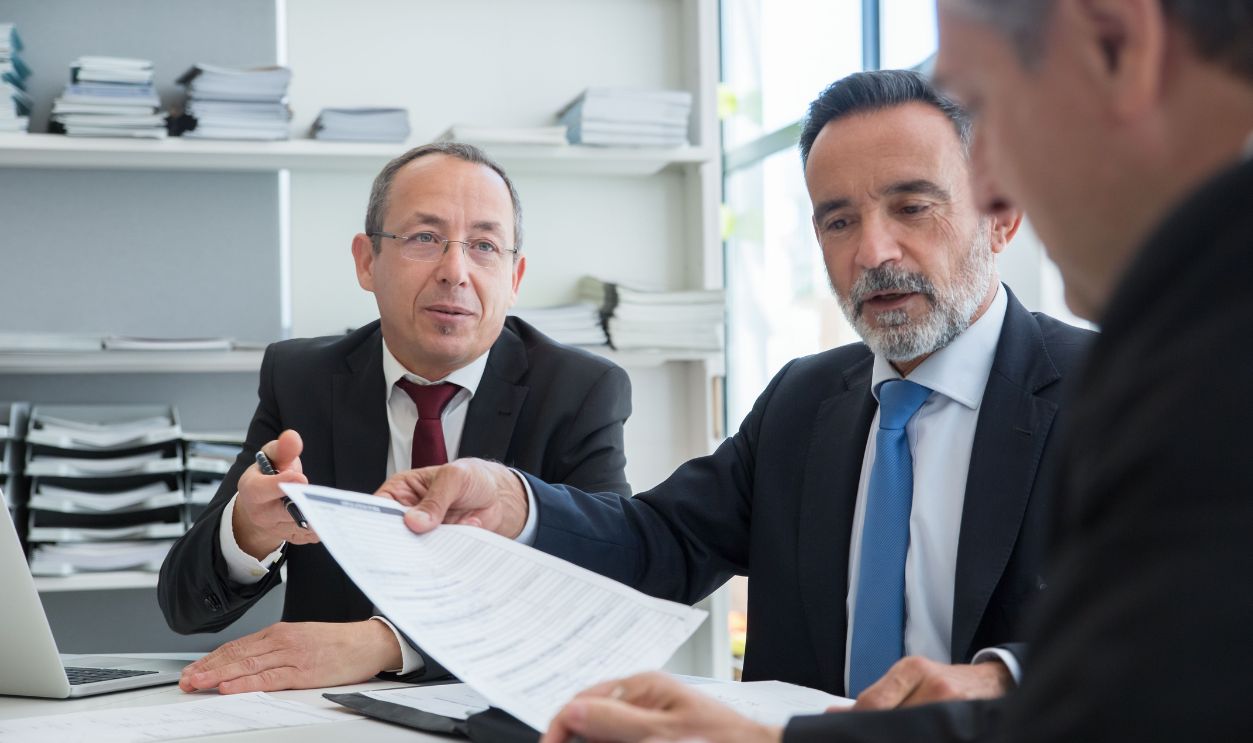 Three businessmen discussing documents in a modern office setting