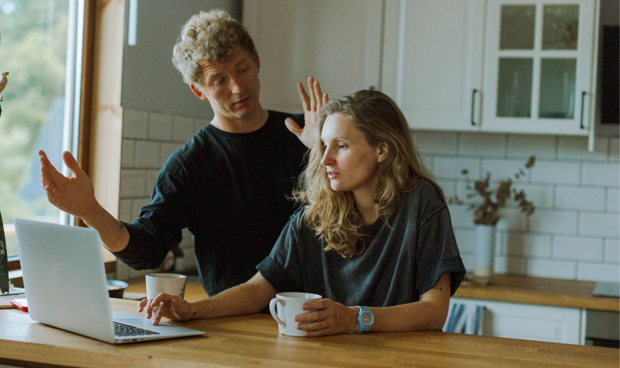 A couple interacting in a bright kitchen using a laptop 